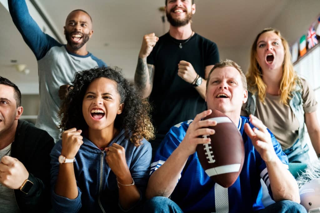 Group of friends watching football in a home together, cheering. Super Bowl