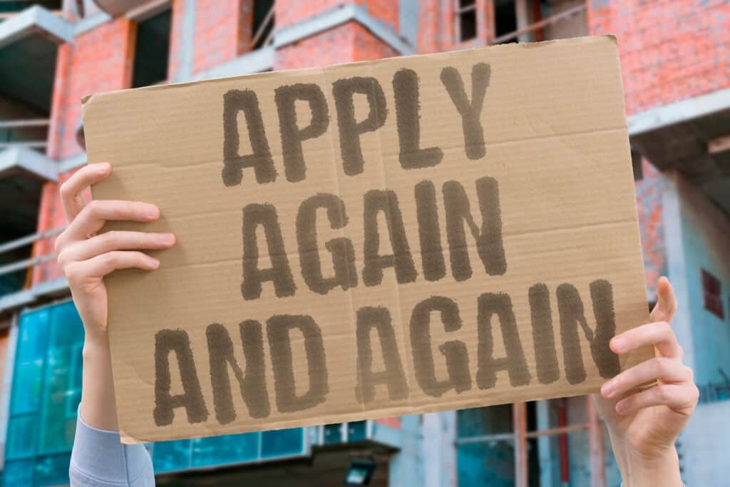 Sign being held up that says "apply again and again"